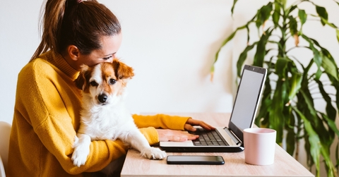 Woman holding dog while she's using a laptop