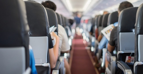 The aisle of an airplane. Passengers fill the seats. 