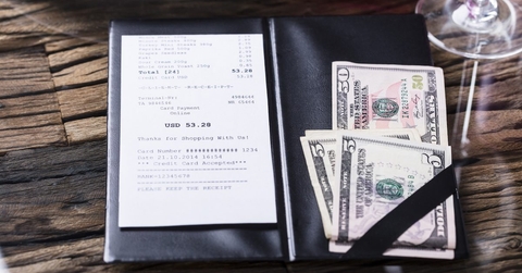 A restaurant bill with a cash tip set to the side. 