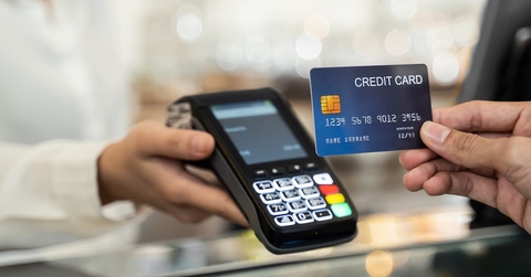 A credit card is held up to a handheld credit card reader. This appears to be at a store checkout.