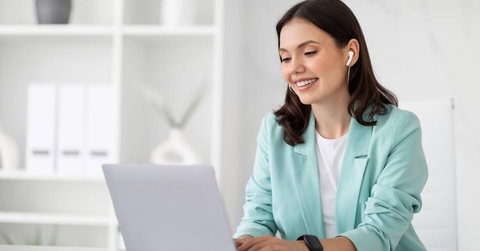A woman typing on her computer and wearing a set of earbuds. 
