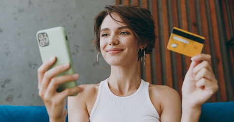 Woman holding a phone in one hand and a credit card in the other