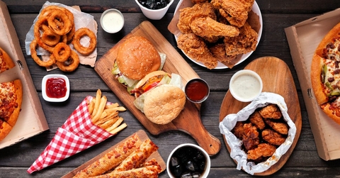 Table scene of assorted take out or delivery foods. Hamburgers, pizza, fried chicken and sides. Top down view on a dark wood banner background.