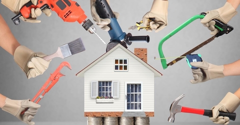 Hands holding up various tools, such as a drill and a paintbrush, around a model of a house that&#x27;s sitting on stacks of quarters.