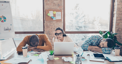 Three coworkers lean over their work table, stressed. 