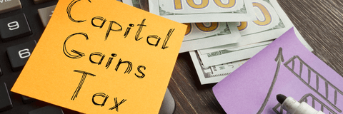 Capital gains tax written on a post-it note next to money