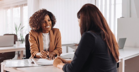 Two women are speaking to each other at a bank.