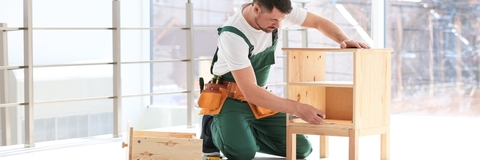Handyperson wearing overalls assembling wooden furniture