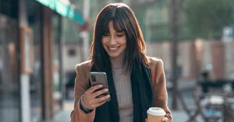 Woman looking at phone and holding coffee