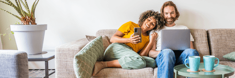 Young couple sitting on couch looking at phone and laptop