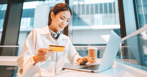 Gen Z woman at cafe on laptop wth debit card in hand