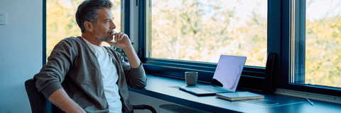 Man thinking with laptop near window