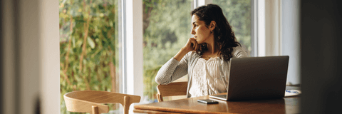Woman thinking near window with her computer