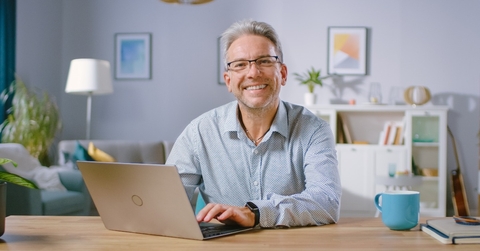 middle-aged man uses laptop computer and smiles on camera