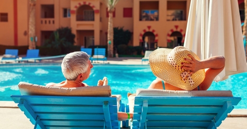 senior couple relaxing on chaise lounges besides a pool