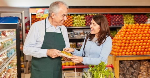 shopkeeper giving vegetables to young female in grocery store
