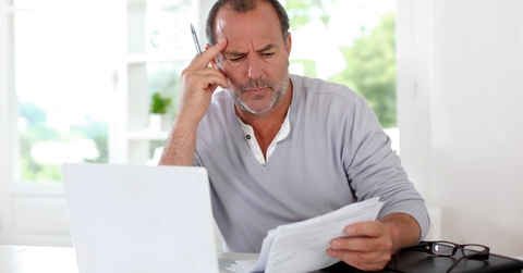 mature man thinking in front of a laptop holding documents