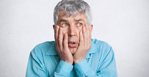 frustrated grey haired male, keeps hands on cheeks