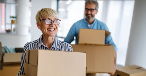 senior couple happily moving into house holding moving boxes