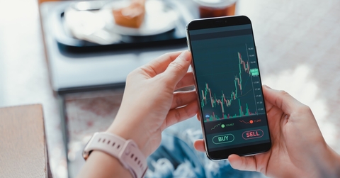 business woman sitting on couch checking stock graphs on smartphone