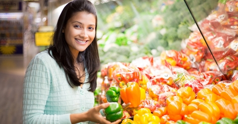 happy woman standing in grocery store buying bell peppers