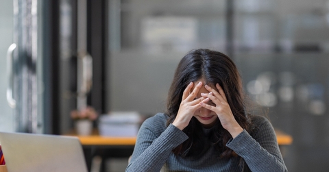 young woman holding head in frustration in front of laptop on table