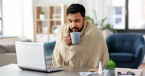 man in blanket with laptop drinking hot tea