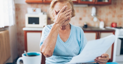 senior woman covering her face in stress while looking at utility bills in kitchen