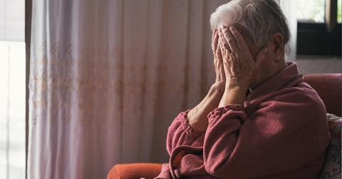 senior lady in depression sitting on couch at home covering her face with hands
