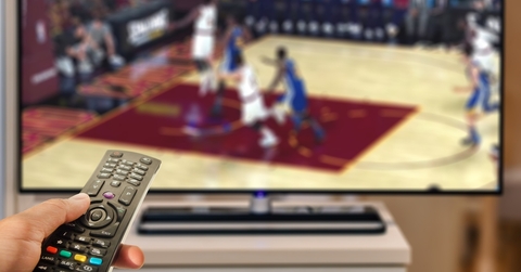 Hand holding a remote in front of a TV playing basketball