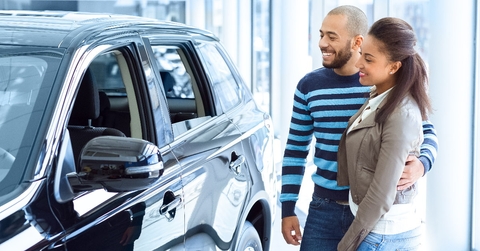 happy couple standing in car showroom checking out new car