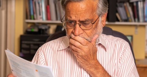 senior man looking at utility bills and covering face in terror