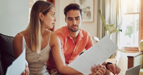 couple sitting on couch arguing over finance and taxes holding papers in hand at home