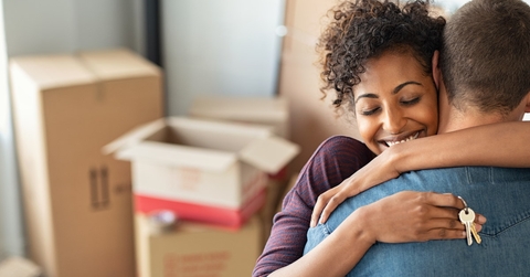 woman hugging man while holding keys with moving boxes in background