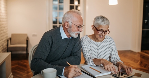 senior couple sitting at wooden table with papers and calculator sorting finances at home for vacation