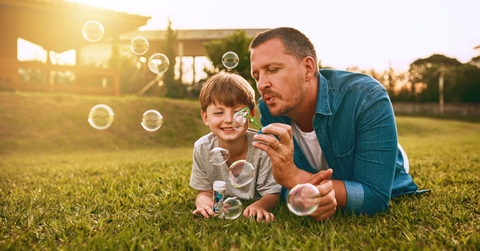 father and son leaning on lawn outdoors playing together while blowing bubbles