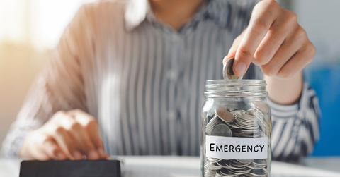 woman putting pennies in glass jar with emergency label on it while using calculator to finance mortgage bills