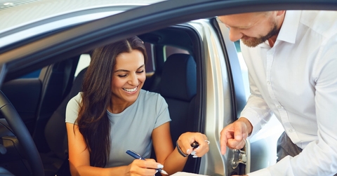 happy woman sitting in new car at car showroom signing papers