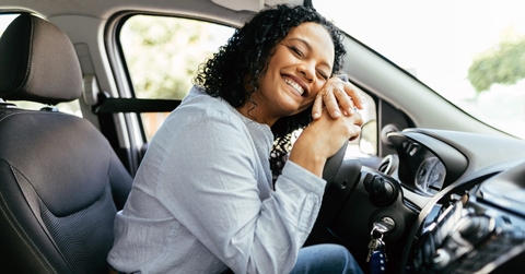 woman sitting at drivier&#x27;s seat wearing seat belt hugging steering wheel