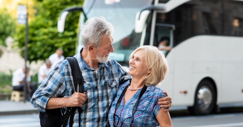 happy senior couple hugging each other on road with tourist bus in background