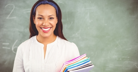 smiling school teacher holding books in classroom
