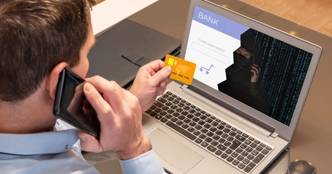 man using laptop holding card while talking on smartphone and getting scammed
