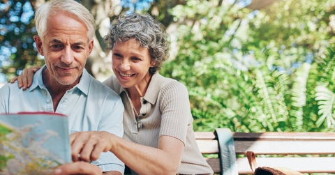 senior couple looking at map in hand while sitting on bench 