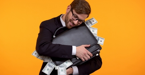 businessman wearing suit hugging briefcase full of money over orange background