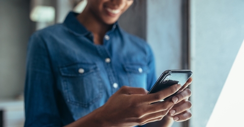 african american woman wearing denim jacket smiling while using smartphone at work