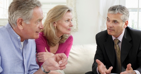 senior couple sitting on sofa with male financial advisor discussing documents
