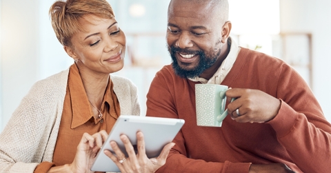african american couple sitting at table reviewing finance using tablet while drinking tea from cup