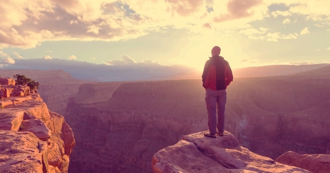 man standing on edge while hiking alone on grand canyon on sunny day