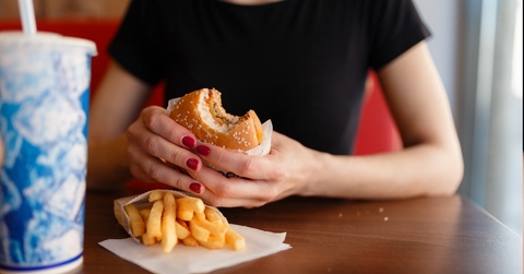 young woman wearing black t-shirt eating burger with fries and cola drink.