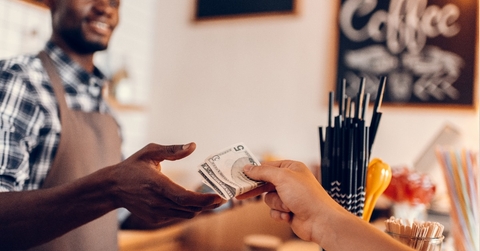 Smiling african american barista taking cash payment from customer on bar counter in cafe.